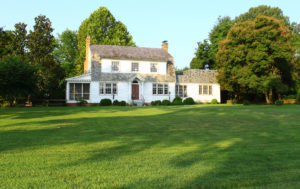 White historic house with a slate roof, surrounded by lush green lawn and mature trees.